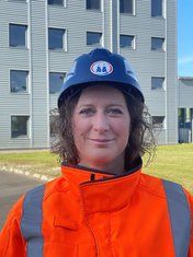 Sandra Bormann, bioprocess engineer and application specialist at Pfeifer & Langen, standing in front of the company building, wearing working clothes and a safety helmet with the company logo.