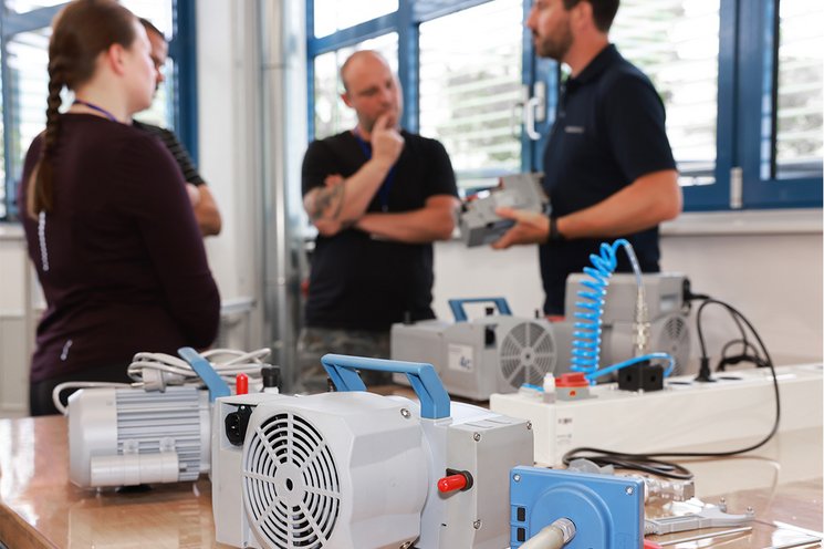 Group of attendees (male and female) at a VACUUBRAND service seminar with vacuum expert. Vacuum pumps on a workbench in the fromt.